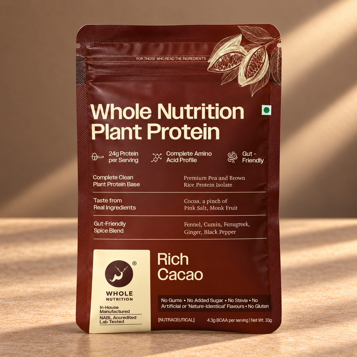 A stand-up pouch of Whole Nutrition Plant Protein in Rich Cacao flavor, shown on a warm beige surface with soft sunlight and shadows. The packaging is dark brown with white text and a cream-colored brand label at the bottom left.