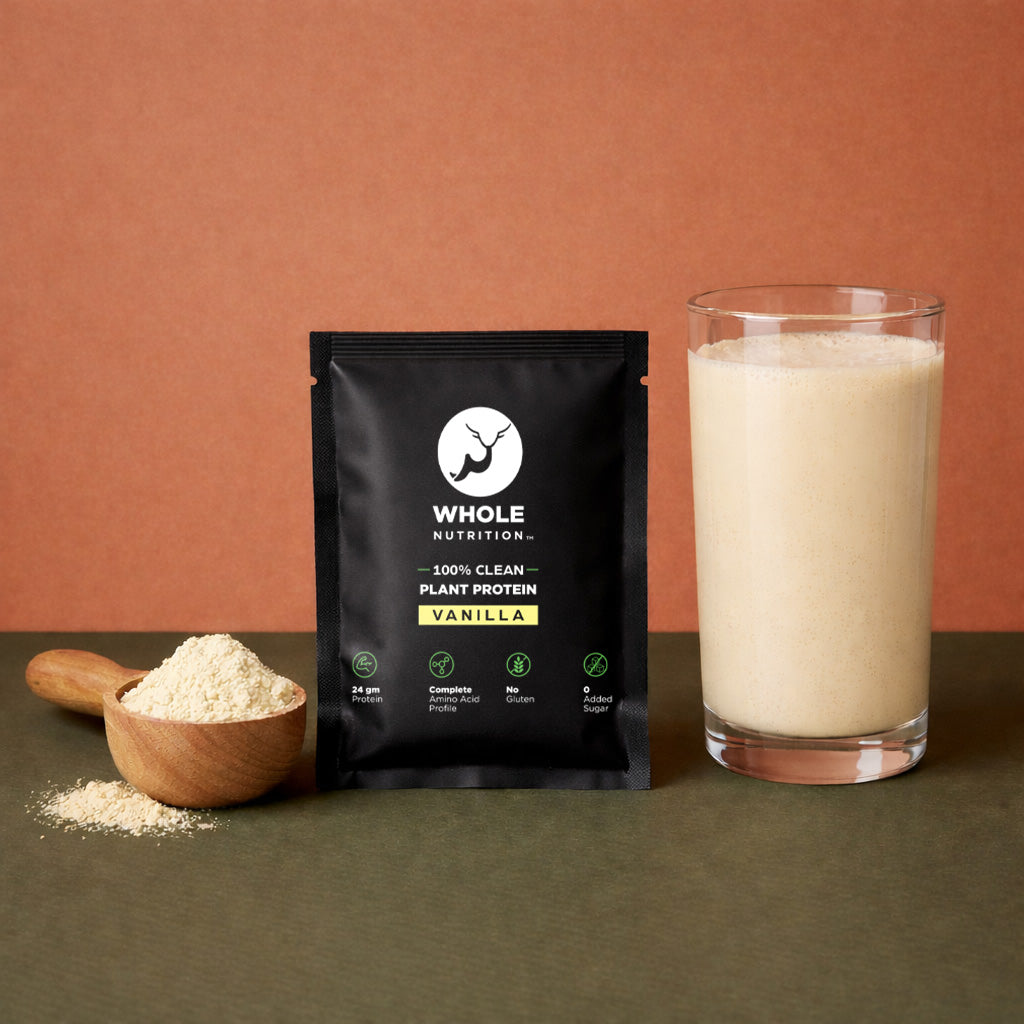 Black package of Whole Nutrition vanilla plant protein with a glass of protein shake and scoop of powder on a brown background.