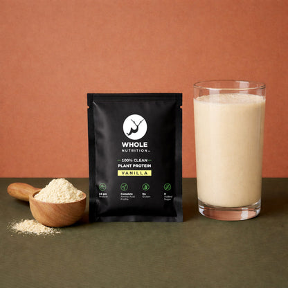 Black package of Whole Nutrition vanilla plant protein with a glass of protein shake and scoop of powder on a brown background.