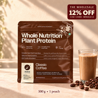 A 500 g pouch of Whole Nutrition Plant Protein Classic Coffee in a brown stand-up package, shown on a warm beige surface with coffee beans and a glass of coffee beside it. A promotional badge in the top right reads 'The Wholesale 12% Off Use Code: Whole12'.