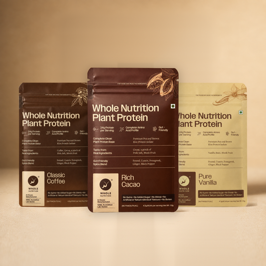 Three Whole Nutrition Plant Protein sachets — Classic Coffee, Rich Cacao and Pure Vanilla — standing side by side on a warm beige surface.